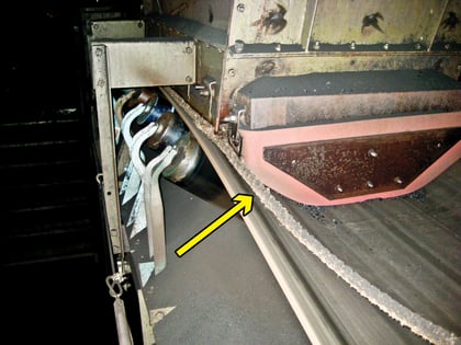 A view of the tail-end of a conveyor with an arrow pointing to a strip of belting that had been laid next to the chute wall to act as sealing.