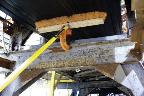 A homemade belt cleaner showing a pushbroom propped up against the return side of the belt.