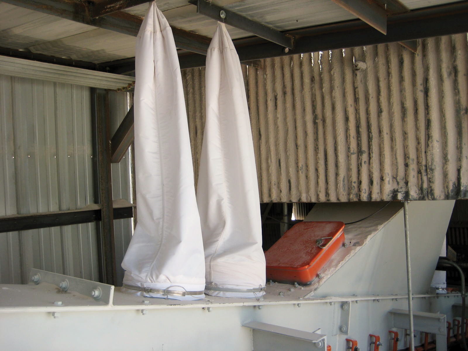 Two dust bags are installed on a transfer point and connect to the ceiling above.